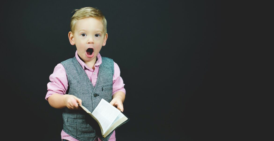 boy wearing gray vest and pink dress shirt holding book