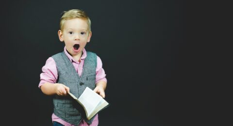 boy wearing gray vest and pink dress shirt holding book